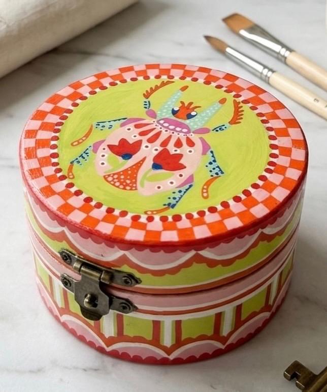 A round wooden trinket box, lid painted with a folk scarab beetle on a lime-green ground.