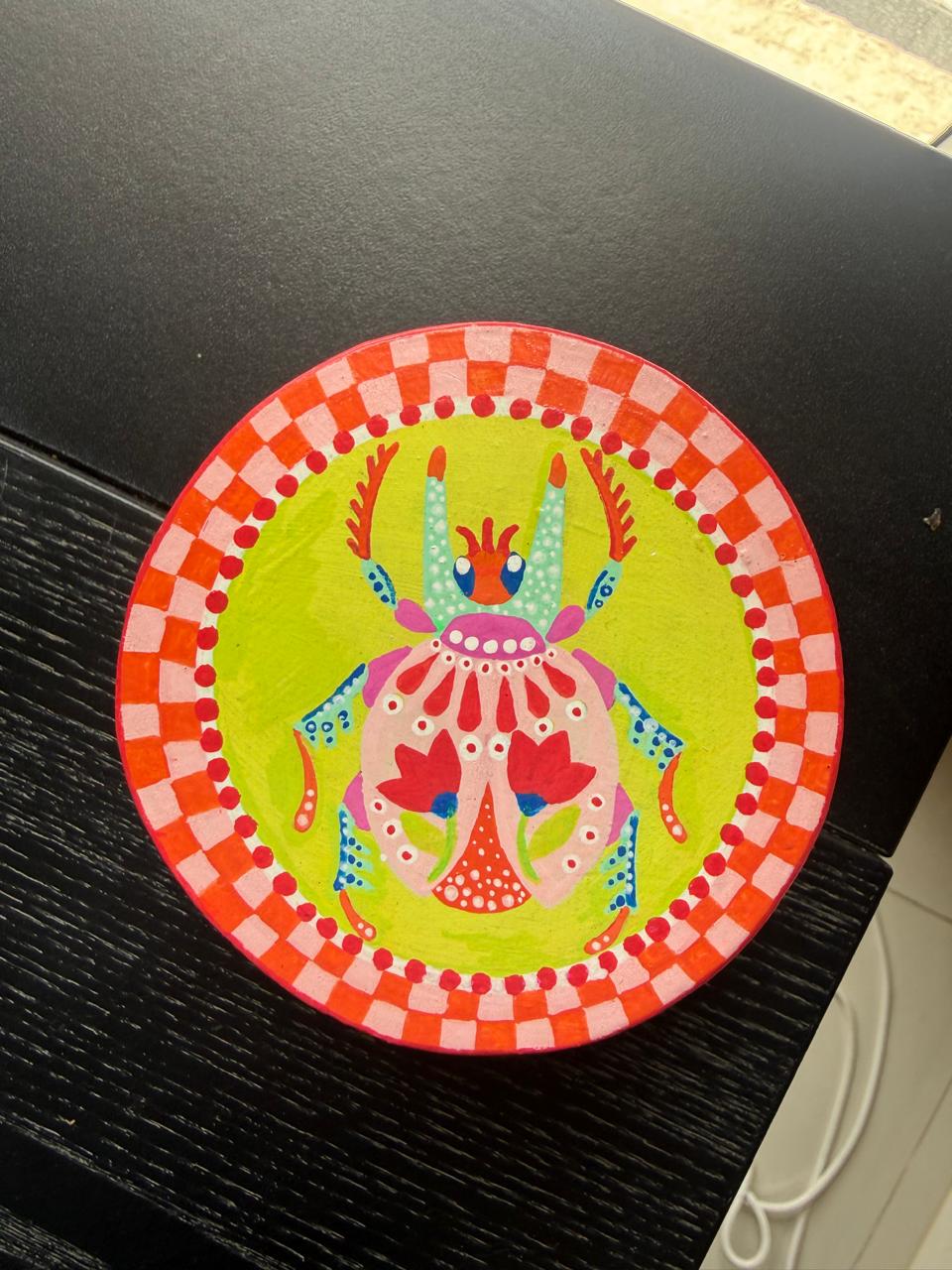A round coaster painted with a folk scarab beetle on lime green, on a dark table.